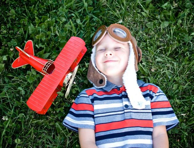 happy child lies on the grass next to a red toy airplane.
